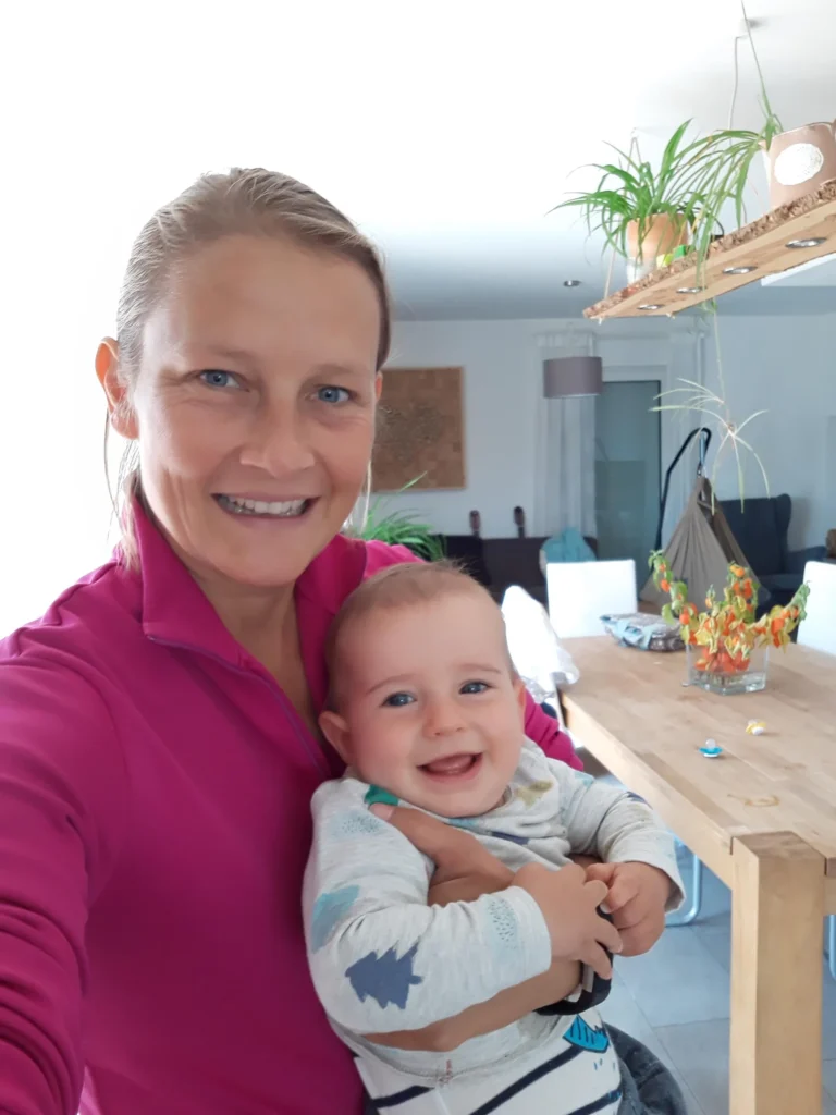 Dr. Kerstin Ott laechelnd mit einem Baby auf dem Arm in ihrem Wohnzimmer